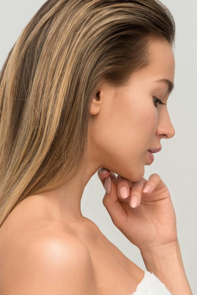 A beautiful woman's profile as she touches her neck, a reflection of the snatched neckline that could be achieved from a neck lift with Dr. Randall, a facial plastic surgeon, in Morristown, NJ